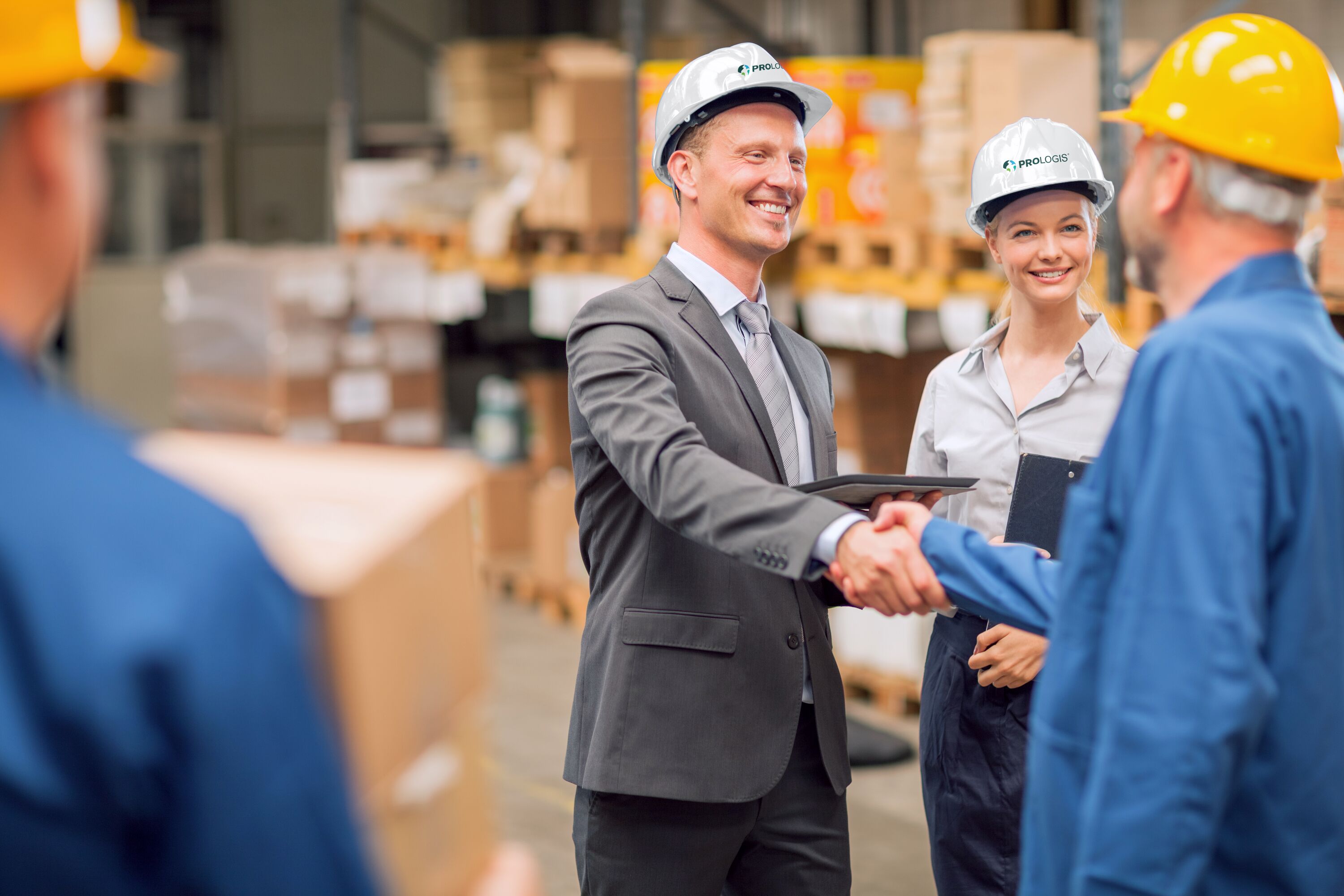 A man and a woman in Prologis hard hats shake hands with 2 warehouse workers