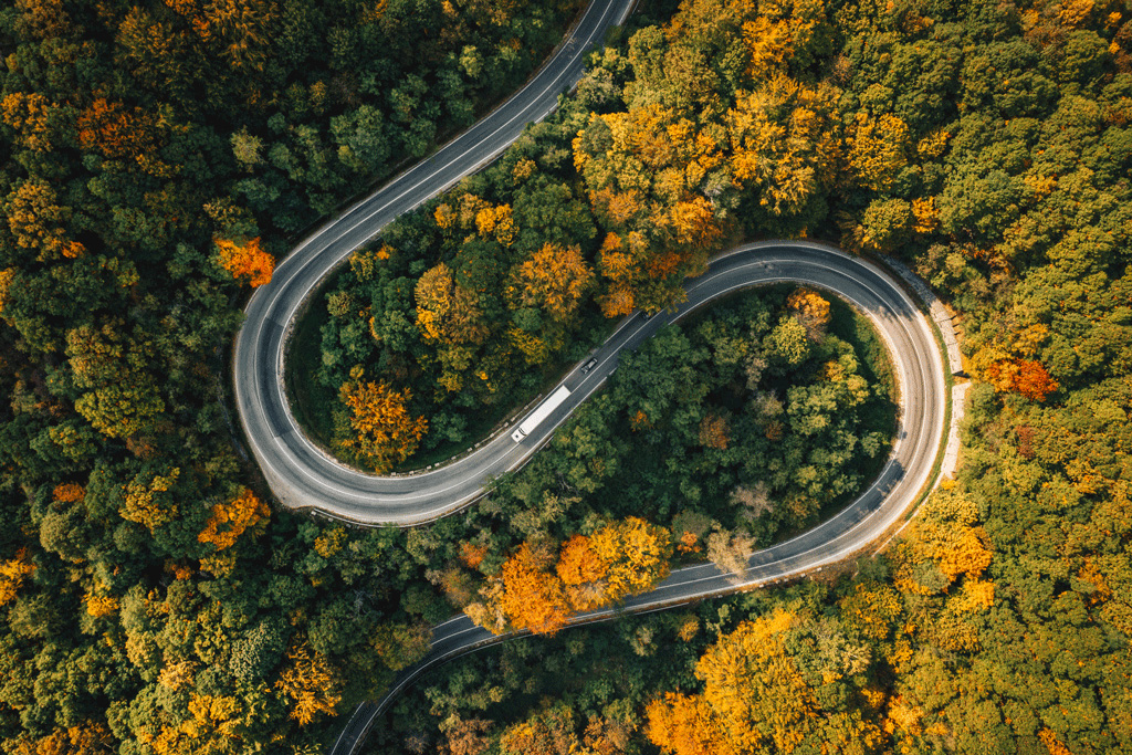 An electric truck driving on a winding road through fall trees