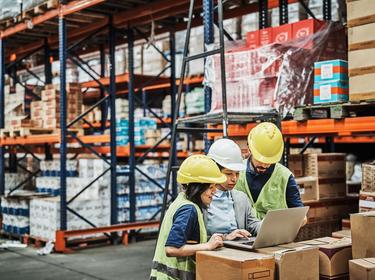 A team of three people working on a laptop in a warehouse