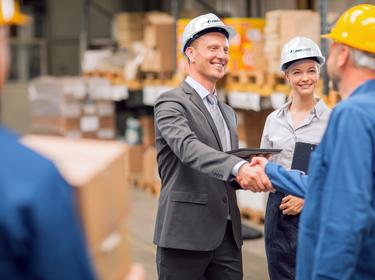 A man and a woman in Prologis hard hats shake hands with 2 warehouse workers
