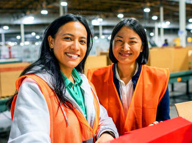 Two women smiling in a warehouse in orange vests